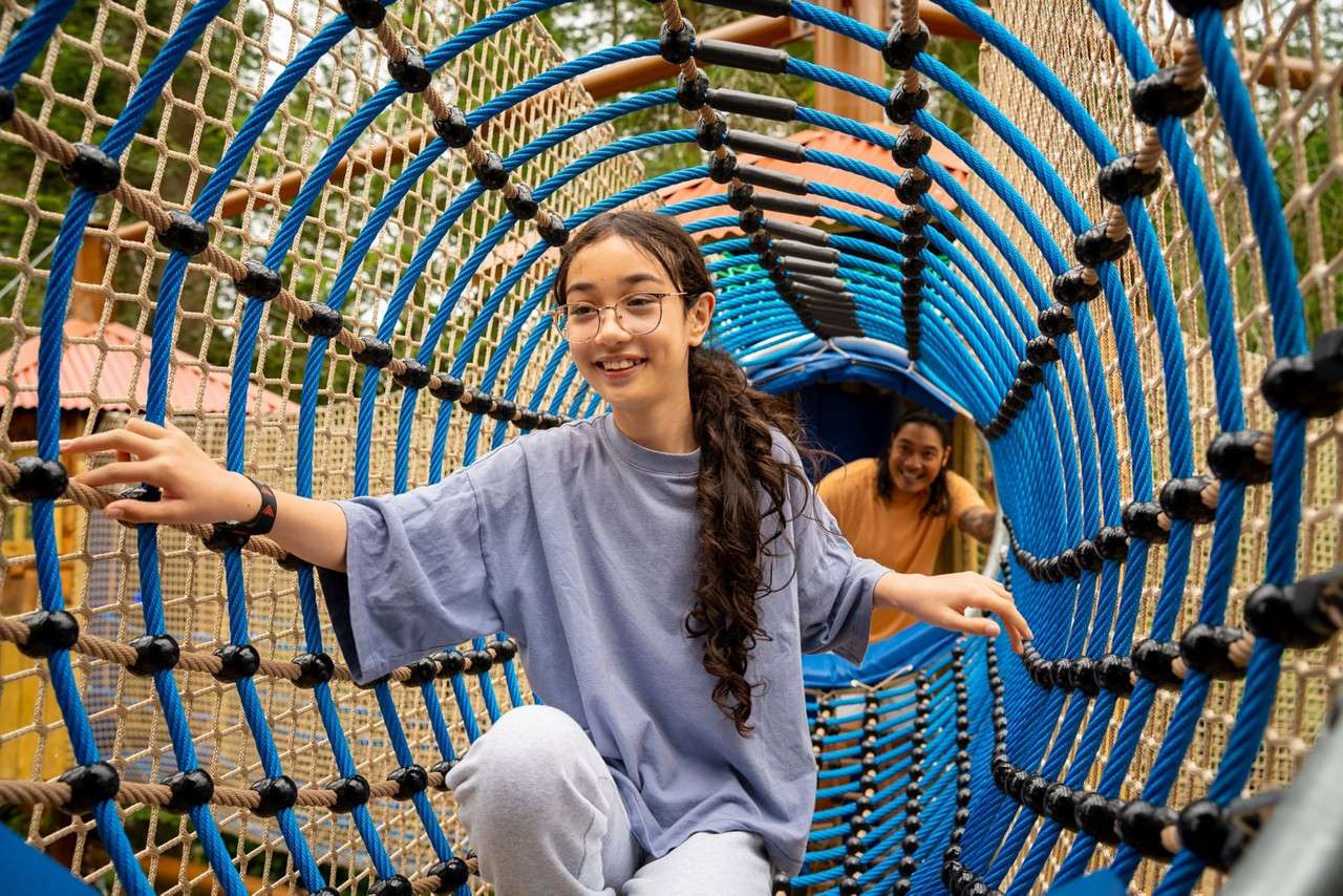 Young girl crawling through a net tunnel.