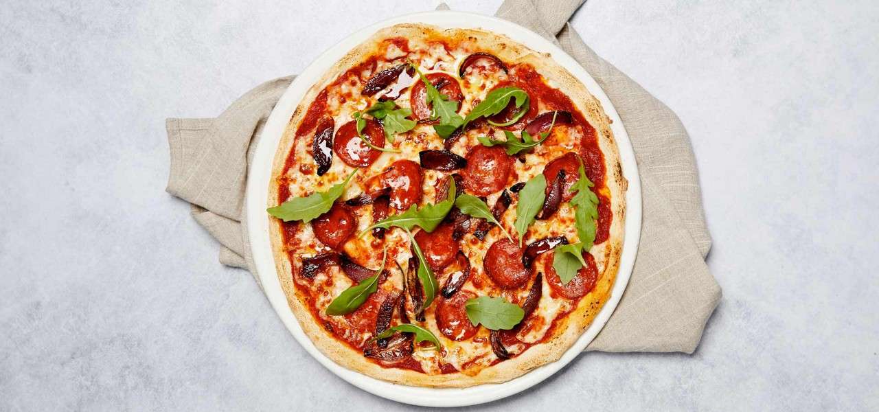 A pizza topped with pepperoni and rocket leaves.