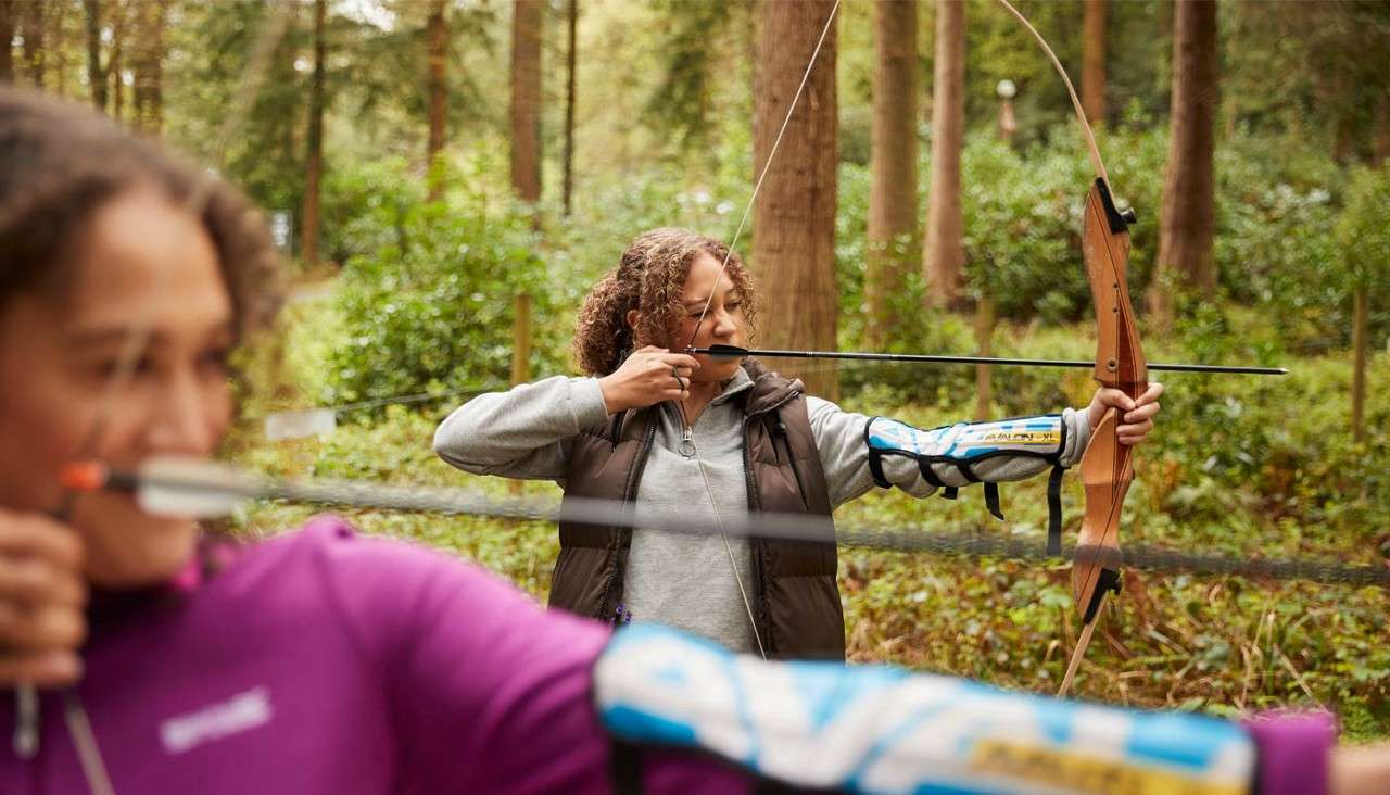 Two ladies doing archery in the forest.