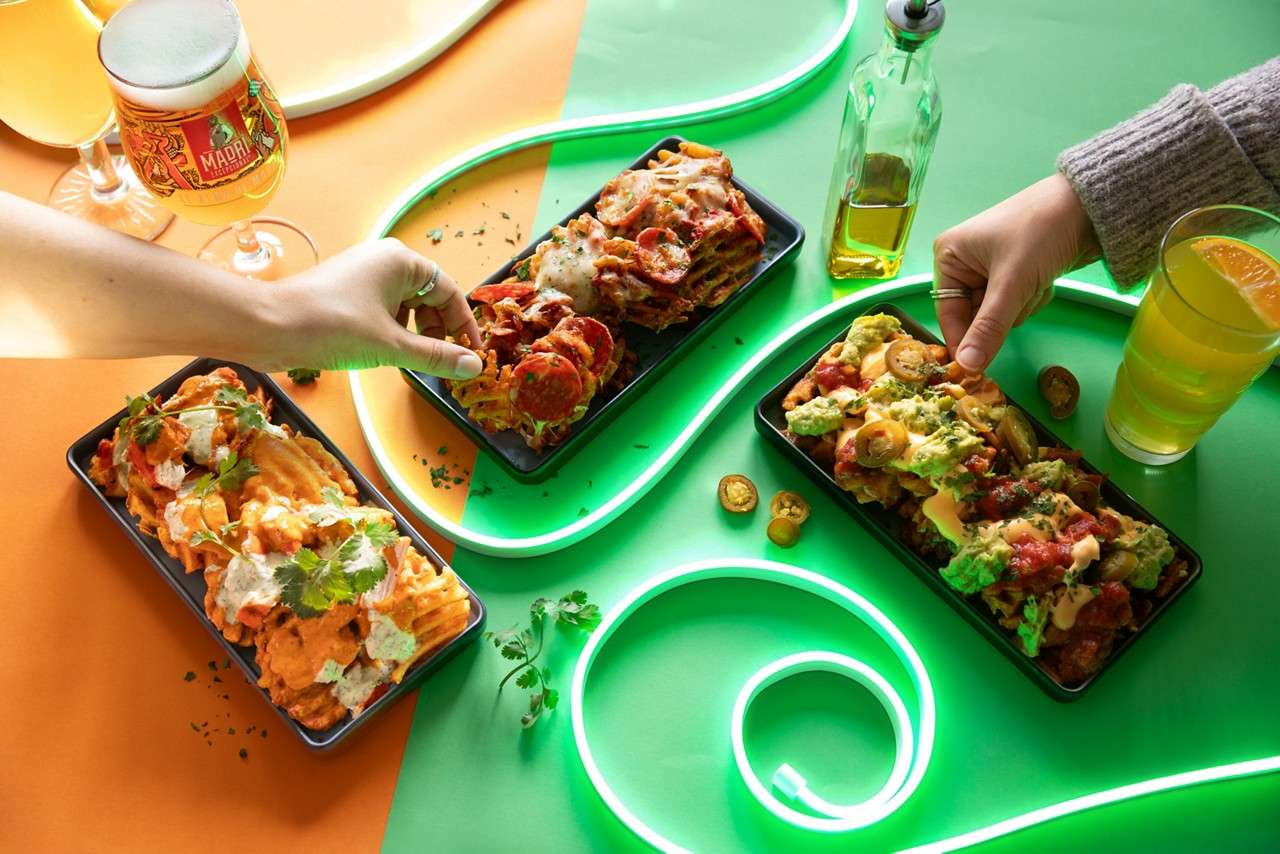 Table decorated with neon lights and people dip into loaded fries.