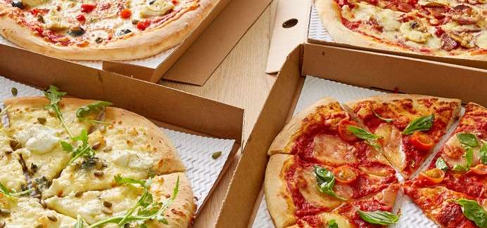 Four open pizza boxes display assorted pizzas—margherita with basil, pepperoni, mushroom, and white pizza with arugula—sliced and ready to serve on a table with corrugated liners.