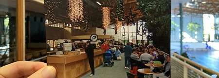 Handheld photo aligns with current space, depicting a busy cafe counter and diners; the atrium behind is brighter and emptier, with plants, big windows, and a sports court beyond railing.